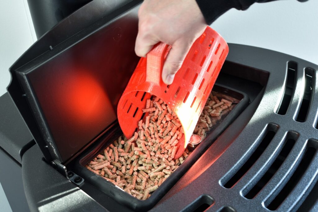 Close-up-on-pellets-black-domestic-pellet-stove-man-loading-by-hand-granules-with-a-red-3-d-printed-cup
